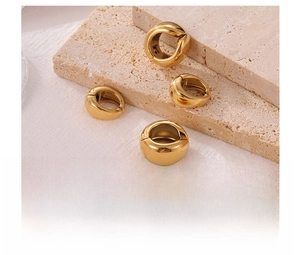 Macro shot of gold vacuum-plated titanium steel clip earrings on a stone textured surface