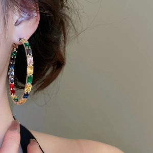 Close-up of a model wearing large gold hoop earrings with colorful zircon gemstones
