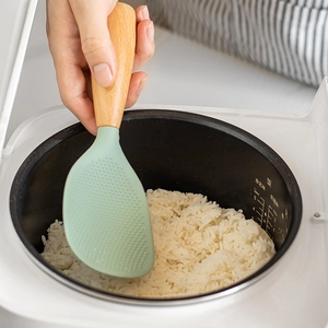 Standing silicone rice paddle with wooden handle and non-stick texture in electric cooker