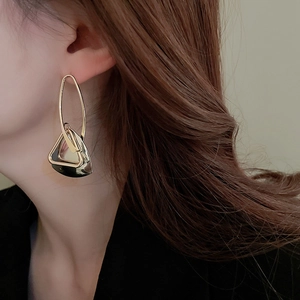 Close-up of golden hollow triangle earrings with oval hoop on woman model ear