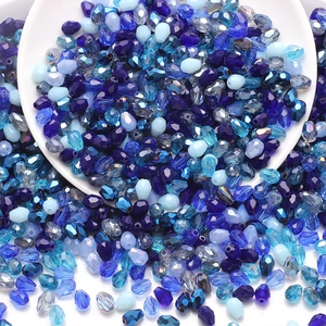 Detail of blue teardrop faceted glass beads scattered from a white ceramic bowl