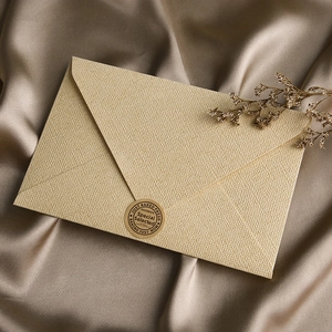 Detailed close-up of linen textured envelope with vintage seal on champagne satin