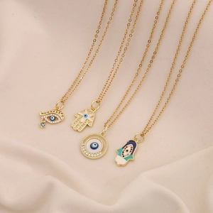 Gold evil eye and Hamsa necklaces with crystal accents on beige fabric background