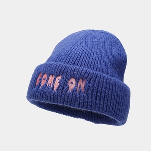 Dettaglio ravvicinato del berretto in maglia blu con ricamo rosa 'COME ON' sul bordo