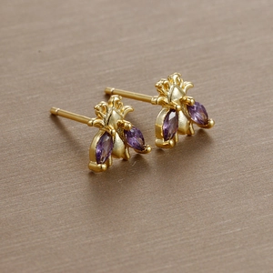 Detailed macro view of gold bee earrings featuring purple marquise-cut crystal wings