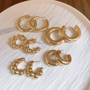 Flat lay of five pairs of gold-plated C-shaped hoop earrings on a ceramic plate