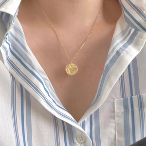 Close-up of a hammered gold compass pendant necklace worn by a model on a striped shirt