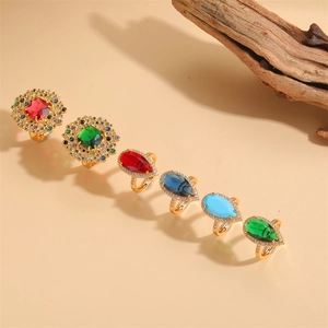 Set of six gold rings with colorful emerald cut zircons on a minimalist wooden background