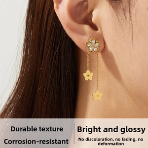 Detail of gold flower drop earrings with crystal pavé and long tassel chains on ear