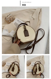 Detail view of round beige crossbody bag with brown leather trim and metal hardware