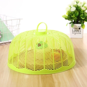 Green round plastic mesh food cover on wooden table protecting fresh fruit bowl