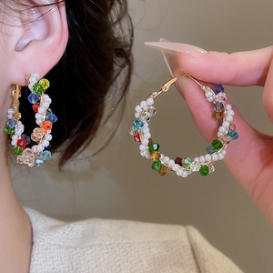 Macro detail of colorful crystal and pearl woven hoop earrings on a golden frame