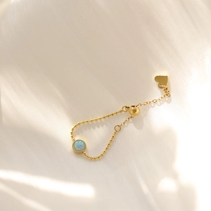 Macro detail of adjustable gold opal ring with bead chain and heart charm