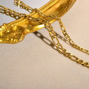 Close-up of golden Figaro chain bracelet with flat links on luxury beige velvet background