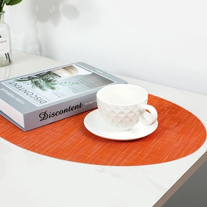 Oval orange bamboo-weave PVC placemat on marble table with a coffee cup and vase