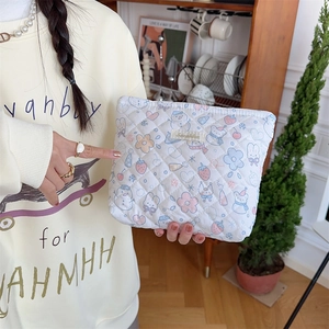 Quilted white cosmetic bag with cute cartoon patterns held by hand in a home setting