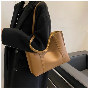 Detail view of large brown leather tote bag showing side profile on black coat model