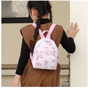 Toddler modeling a light pink cartoon bear backpack showing side view and shoulder straps