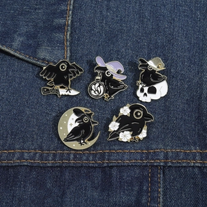 Detailed view of 5-piece black crow enamel pins set on blue denim fabric background