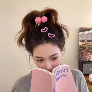 Pink woven ponytail hair tie and heart-shaped clips worn by a model in a cozy setting