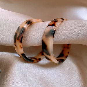 Macro detail of leopard print resin hoop earrings on luxury champagne silk fabric