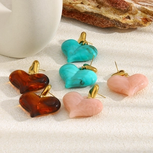 Détail de boucles d'oreilles cœur en acrylique marbré avec clous plaqués or 18 carats en 3 tons