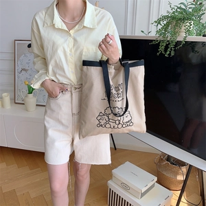 Close-up of beige canvas tote with Lucky Lucky dog embroidery and black woven handles