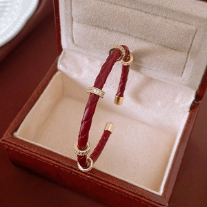 Détail du bracelet en cuir tressé rouge avec accents dorés et cristaux brillants