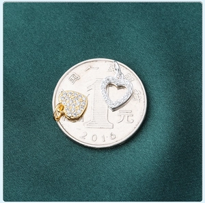 Detailed macro view of S925 silver heart charms with pavé crystals next to a coin