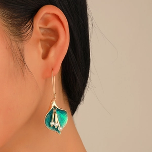 Detailed view of gold calla lily earrings with green enamel and hanging pearls on a model