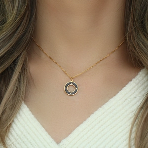 Detail of a gold necklace with a black circular pendant worn on a white sweater