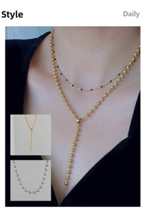 Detail of gold beaded Y-shaped long necklace shown as layered jewelry on person