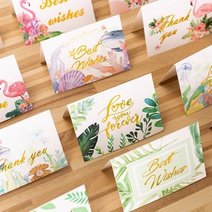 Minimalist gold-stamped greeting cards with tropical and marine designs on wood surface