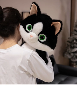 Close-up of a large black and white plush cat with green eyes being held by a model
