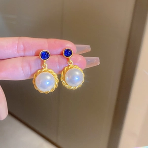 Detailed shot of vintage gold earrings with blue gemstones and white pearls in woven frames