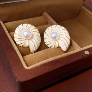 Close-up of shell-shaped gold earrings with cream enamel and a central lavender pearl