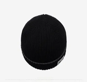 Top view of black ribbed knit beanie featuring a white rectangular woven patch detail