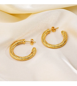 Detail of 18K gold-plated twisted hoop earrings on beige silk fabric background