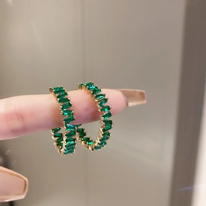 Golden hoop earrings with green rectangular stones worn on fingers in natural light