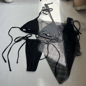 Detailed view of black bikini set with high-waist mesh cover-up on beige carpet