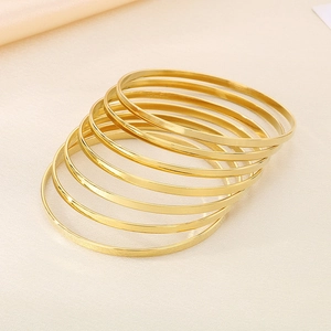 Macro detail of stacked glossy gold thin titanium steel bangles on satin background
