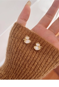 Detailed macro of gold plated gourd stud earrings with zircon held against a brown sweater
