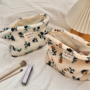 Detail of plush floral cosmetic bags showing soft texture and zipper on white linen