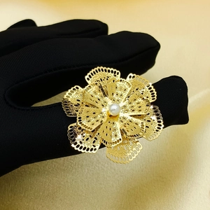 Detail of hollow golden flower ring with pearl center worn on a black glove