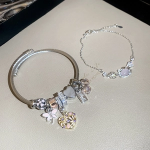 Detail of silver bangle with pink enamel butterfly and crystal heart charms on leather tray