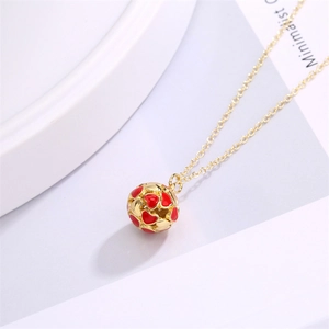 Macro shot of gold-plated ball pendant featuring red enamel hearts on a fine chain