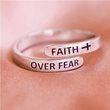Vista macro de un anillo plateado con grabado Faith Over Fear y detalle de símbolo cruz