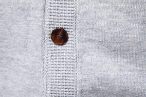 Close-up of light grey knit texture with a dark brown resin button on a men cardigan