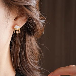 Close-up of golden cloud earrings with teardrop pendants on model's ear