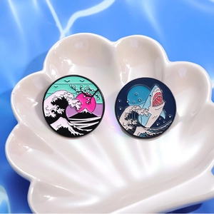 Enamel wave and shark pins on a shell tray with blue rippled water background